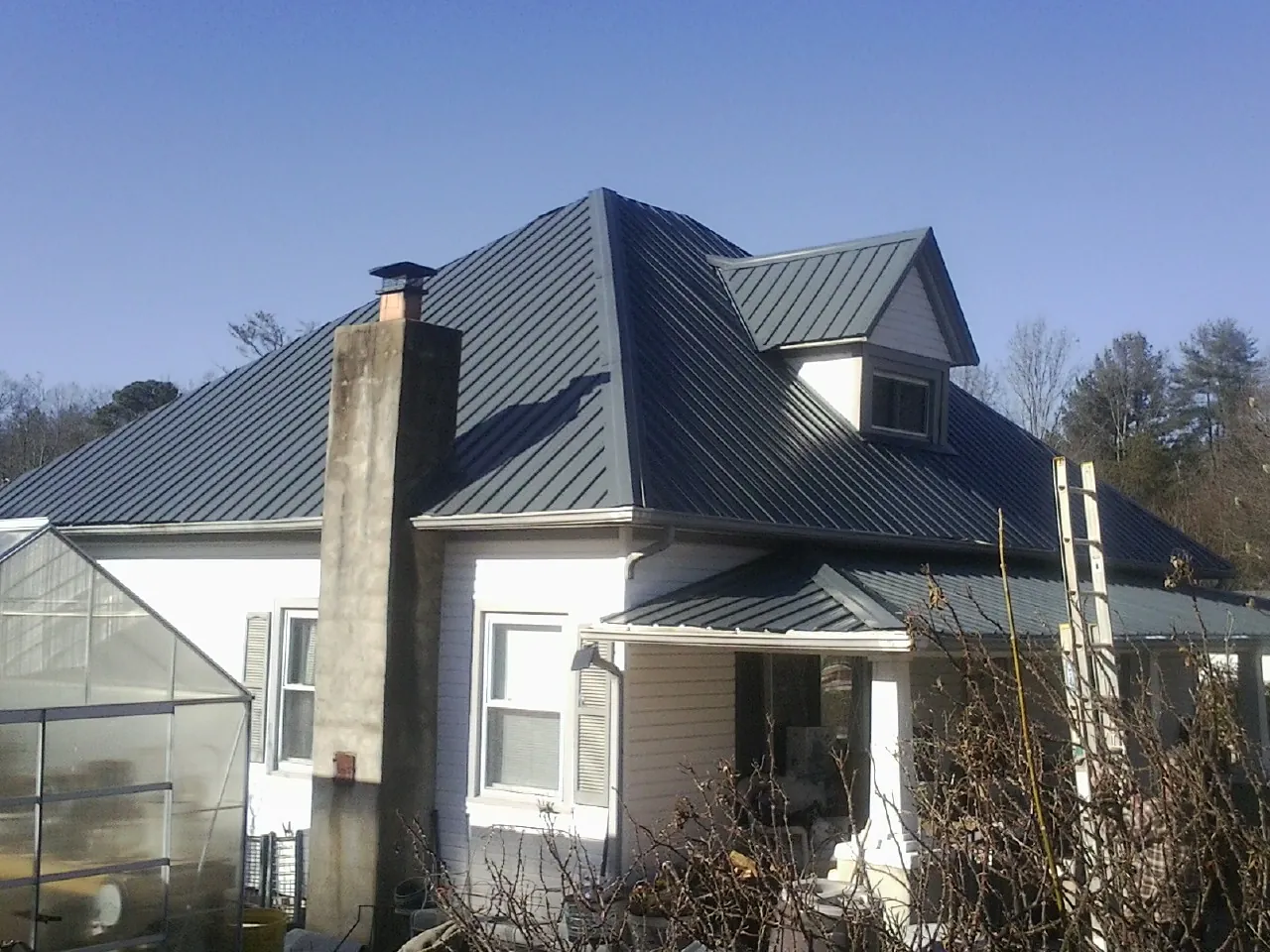 Dark blue standing seam metal roof on a white farmhouse with dormer — Slate & Tile Roof Repair by Roofing Brothers in Amagansett