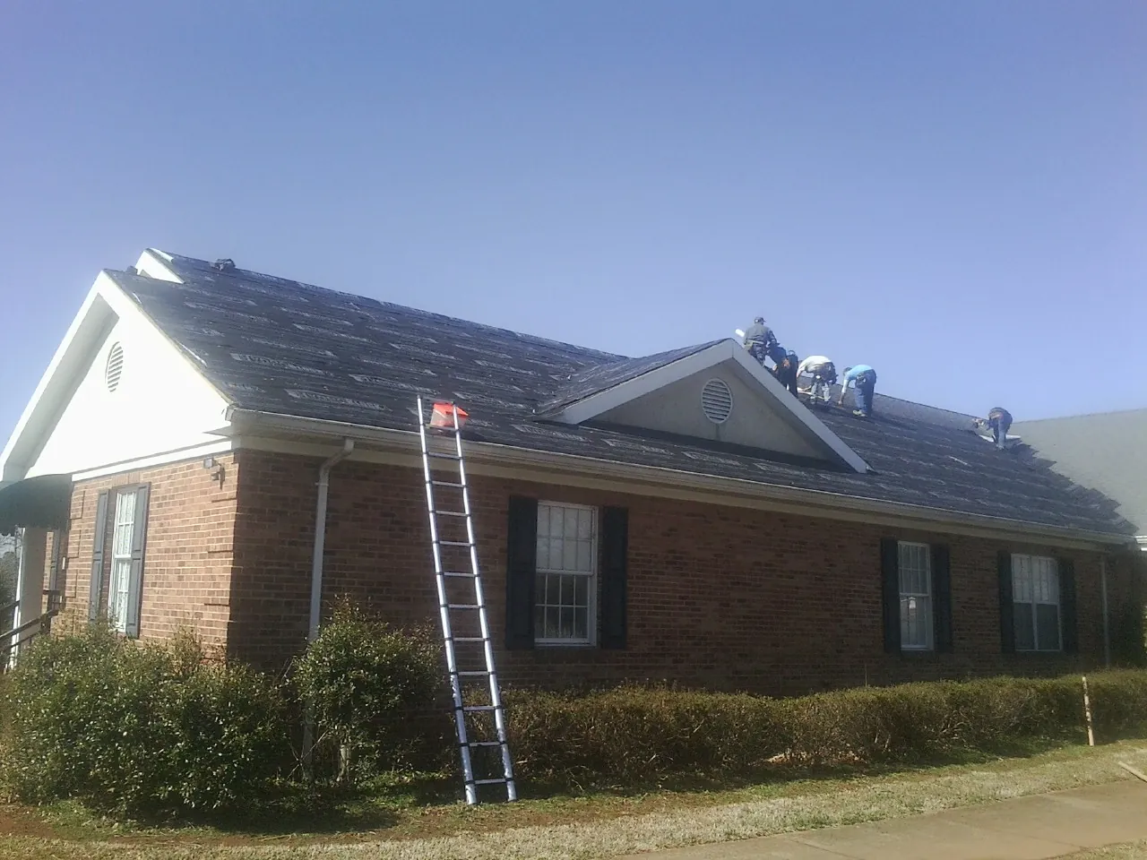 Crew tearing shingles off a brick ranch roof with a ladder set — Metal Roof Repair work by our crew in Amagansett