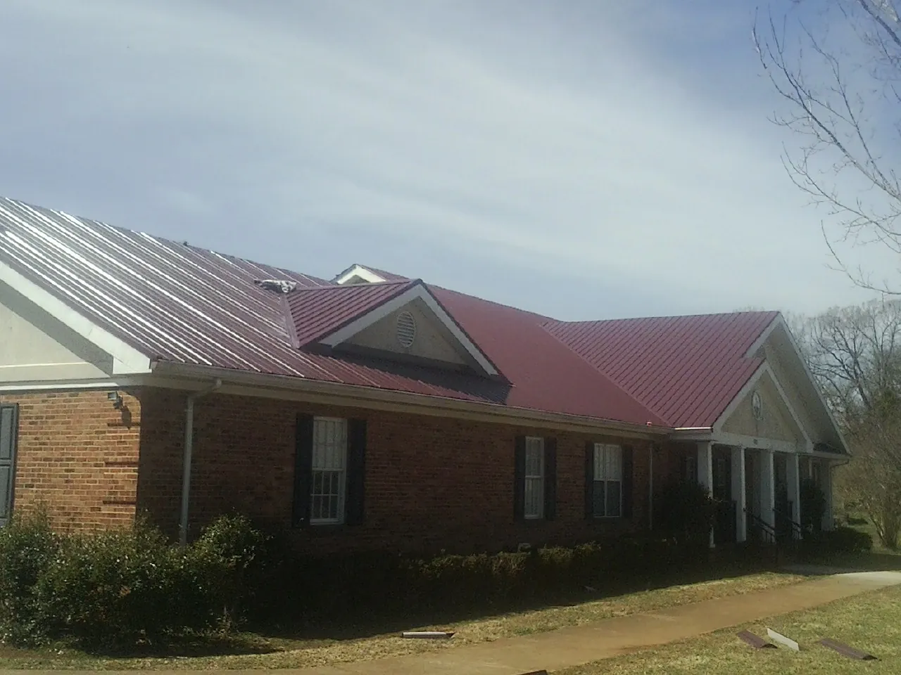Red metal roof with gabled entries on a long brick building, from a Hail Damage Roof Repair job in Amagansett