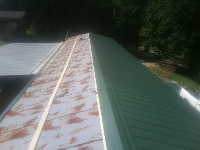 Old rusted panels beside newly installed green metal roofing — Wind Damage Roof Repair by Roofing Brothers in Amagansett
