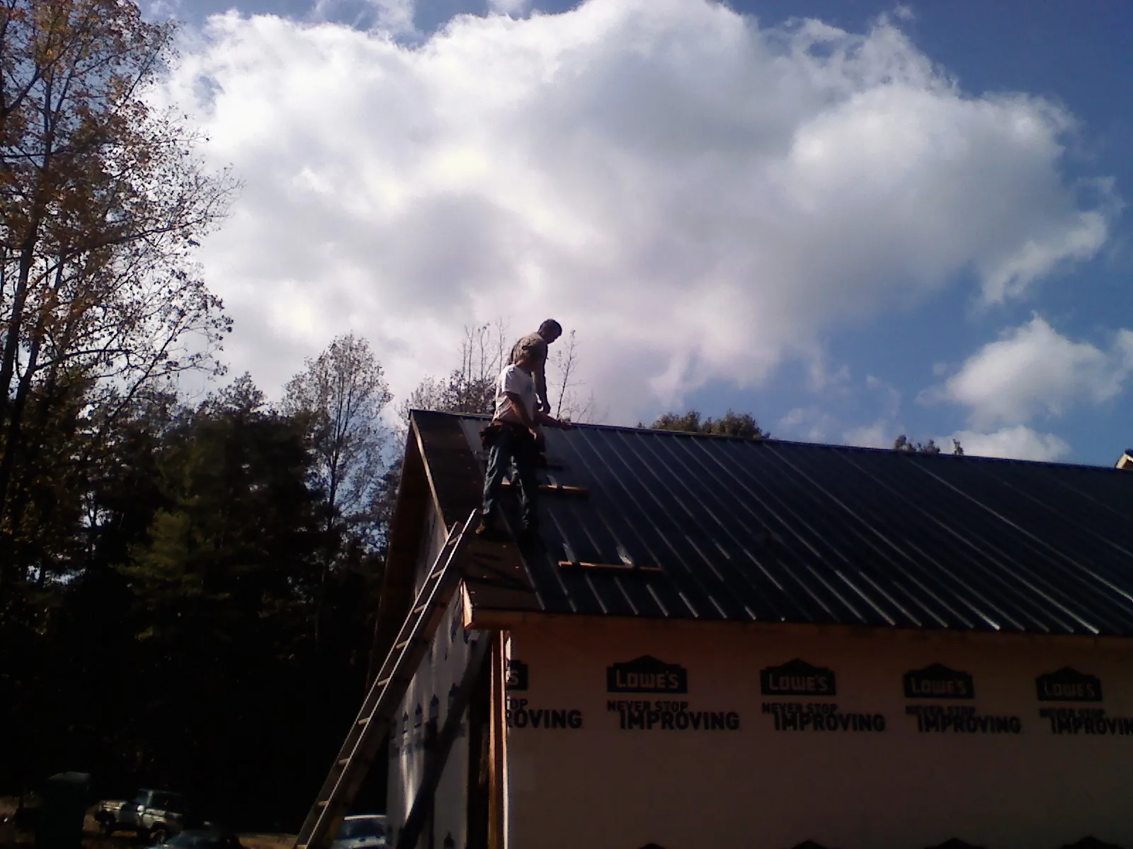 Roofer fastening dark metal panels high against a cloudy sky, from a Roof Inspection job in Amagansett