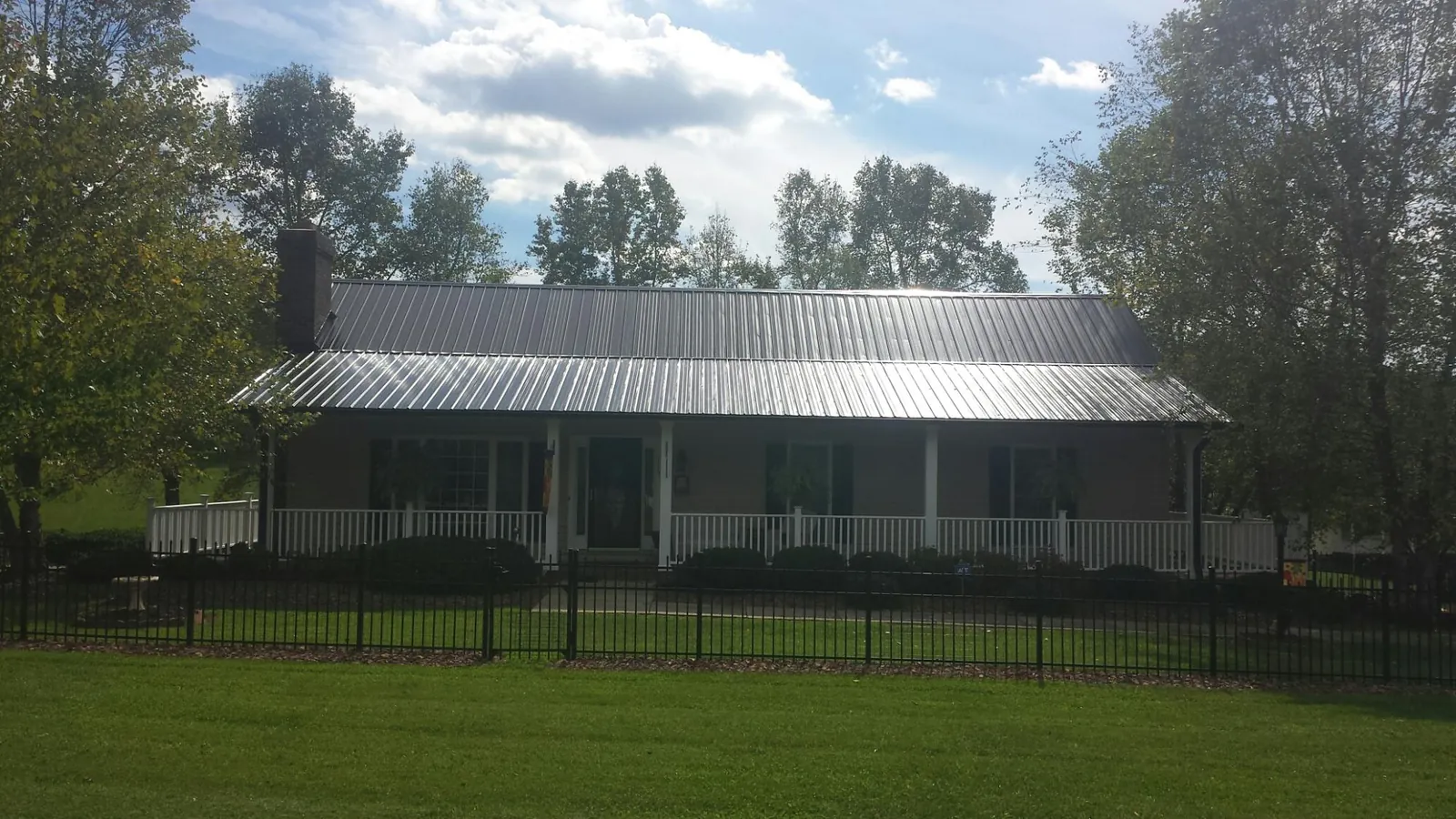 Gray metal roof on a brick ranch with a full width front porch — Gutter Guard Installation work by our crew in Amagansett