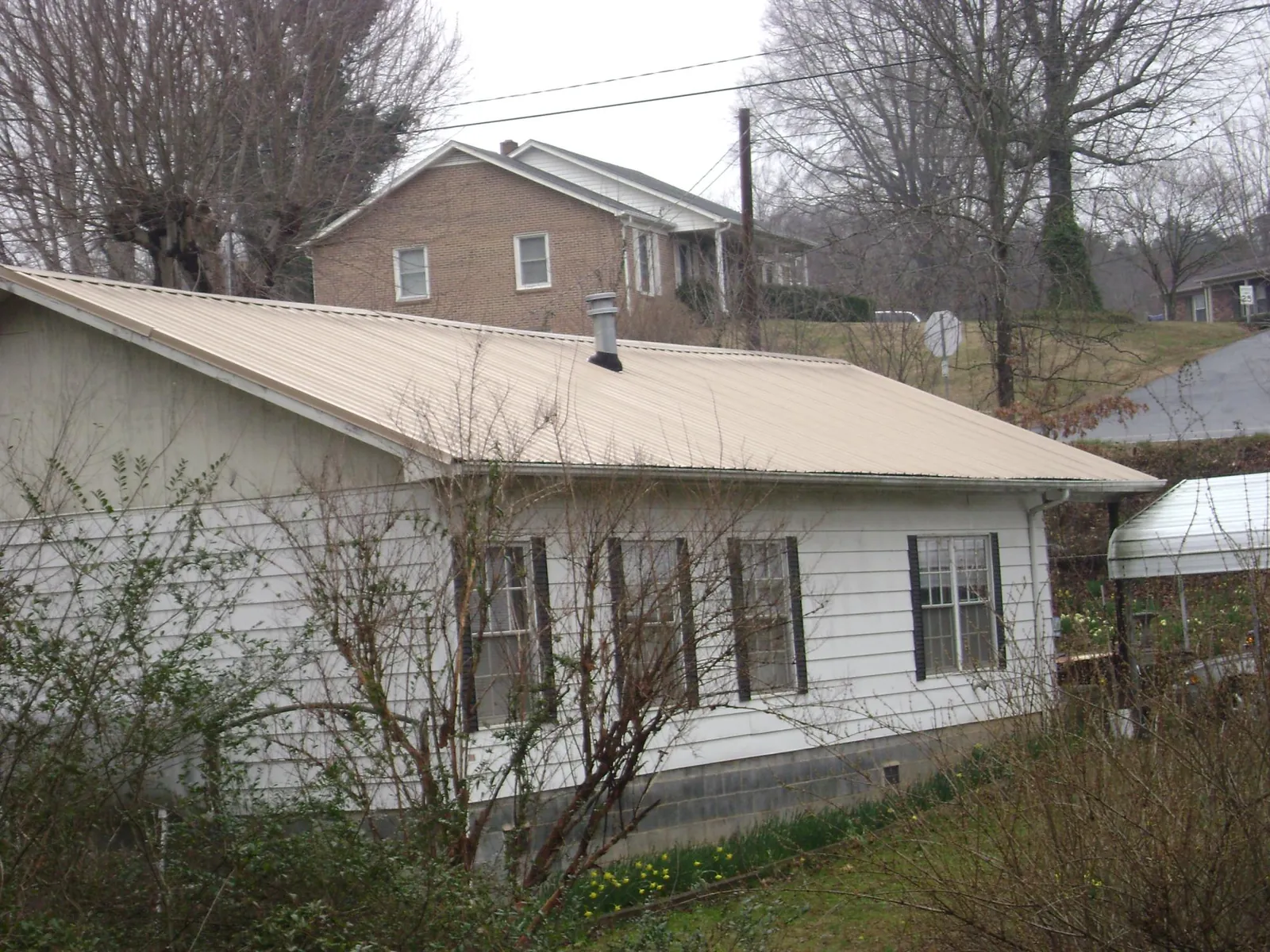 Tan metal roof on a white sided house set into a hillside — Commercial Roofing by Roofing Brothers in Amagansett